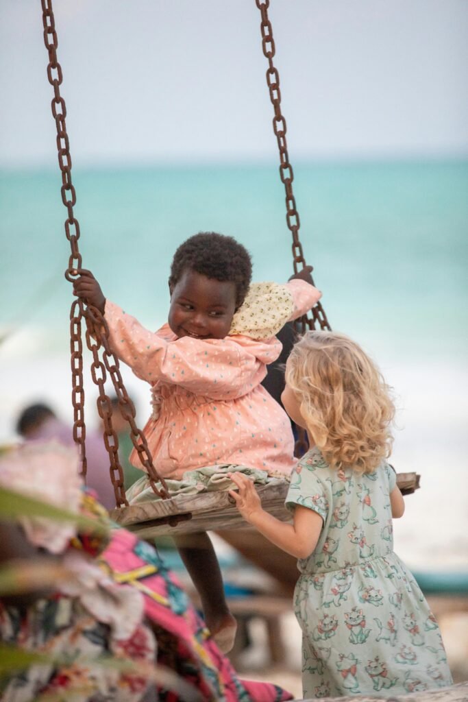 Two children enjoy a playful moment on a swing at a sandy beach in Zanzibar.
